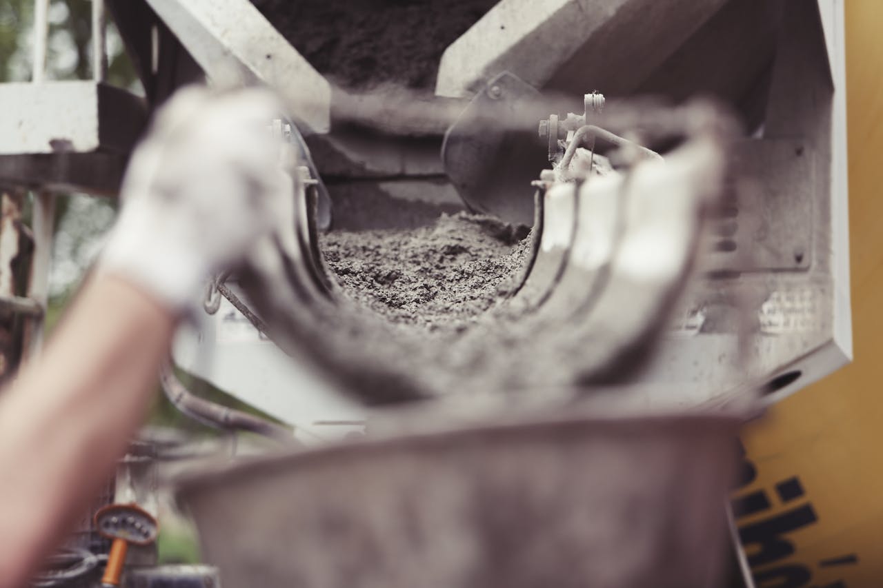 heros-img Close-up of concrete being poured from a mixer truck at a construction site with a worker's hand visible.